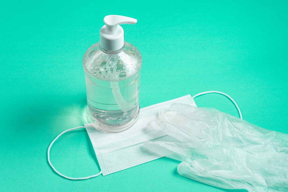 Container with alcohol gel, gloves and surgical mask on the light blue